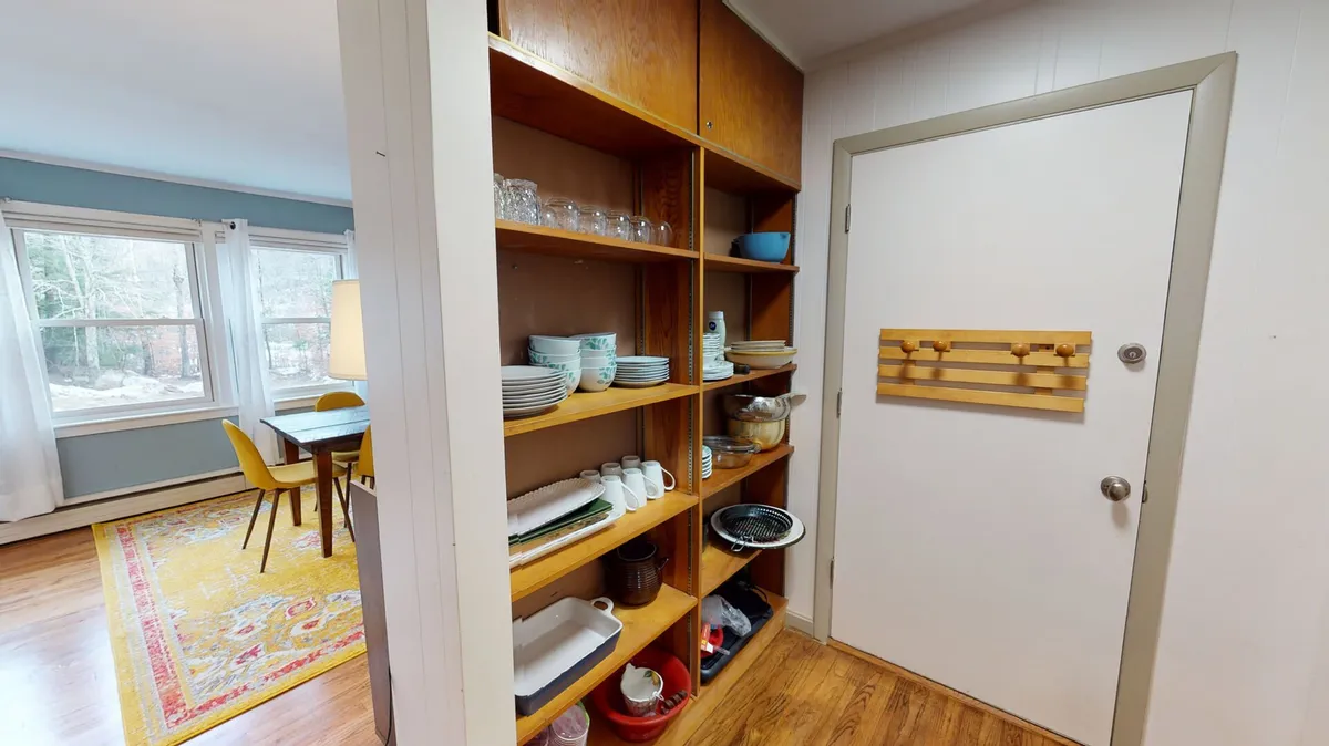 This image features a cozy dining area with a wooden shelving unit, a dining table surrounded by chairs, and a brightly colored area rug. Natural light appears to brighten the space, hinting at a welcoming spot to gather after outdoor activities. The decor exudes warmth, perfect for transitioning from nature exploration to shared indoor moments.