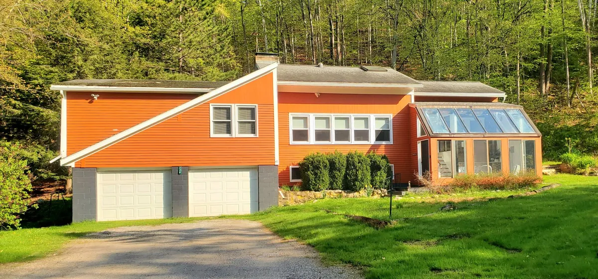 A bright orange exterior of the house with large windows and a sunroom, surrounded by greenery. The scene suggests a welcoming home base after outdoor adventures, with spaces to relax and soak in nature.
