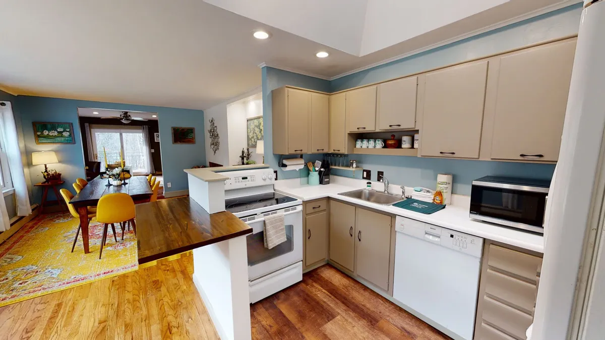This image centers on the kitchen island with bar seating, featuring modern appliances. In the background, the adjoining dining area is visible, seamlessly connecting the two spaces. The overall atmosphere is bright, comfortable, and welcoming—ideal for culinary activity and social gatherings.