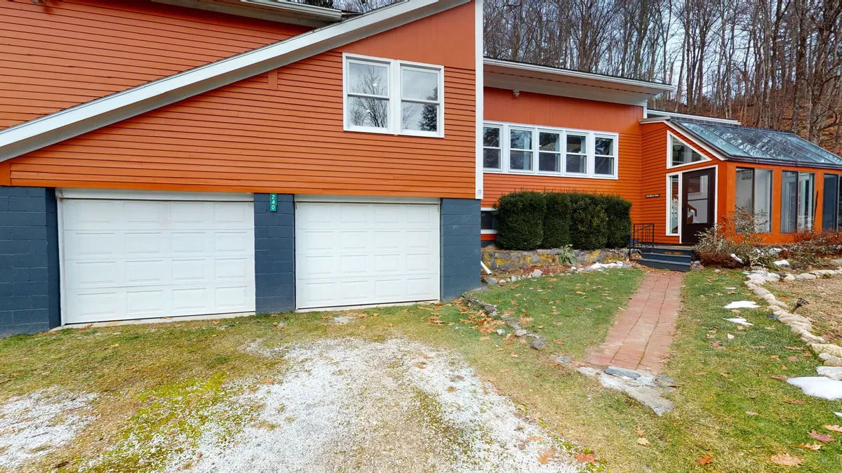 A welcoming exterior view of the home, featuring an orange facade, large windows, and two garages. The front area is spacious and inviting, hinting at the ample outdoor spaces available for gatherings and relaxation.
