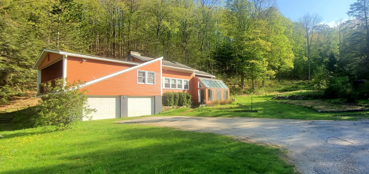 A view of the house set against lush greenery, with modern architecture, large windows, and a driveway leading to the entrance. The scene conveys accessibility to outdoor activities and a peaceful, inviting atmosphere, perfect for returning to after a day of exploration.