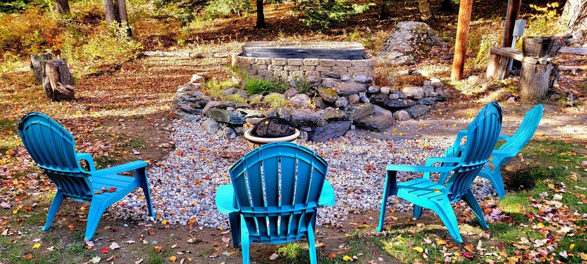 A communal fire pit surrounded by blue chairs and natural stone, set against a backdrop of vibrant fall foliage. The setting is ideal for evening gatherings and making s'mores.