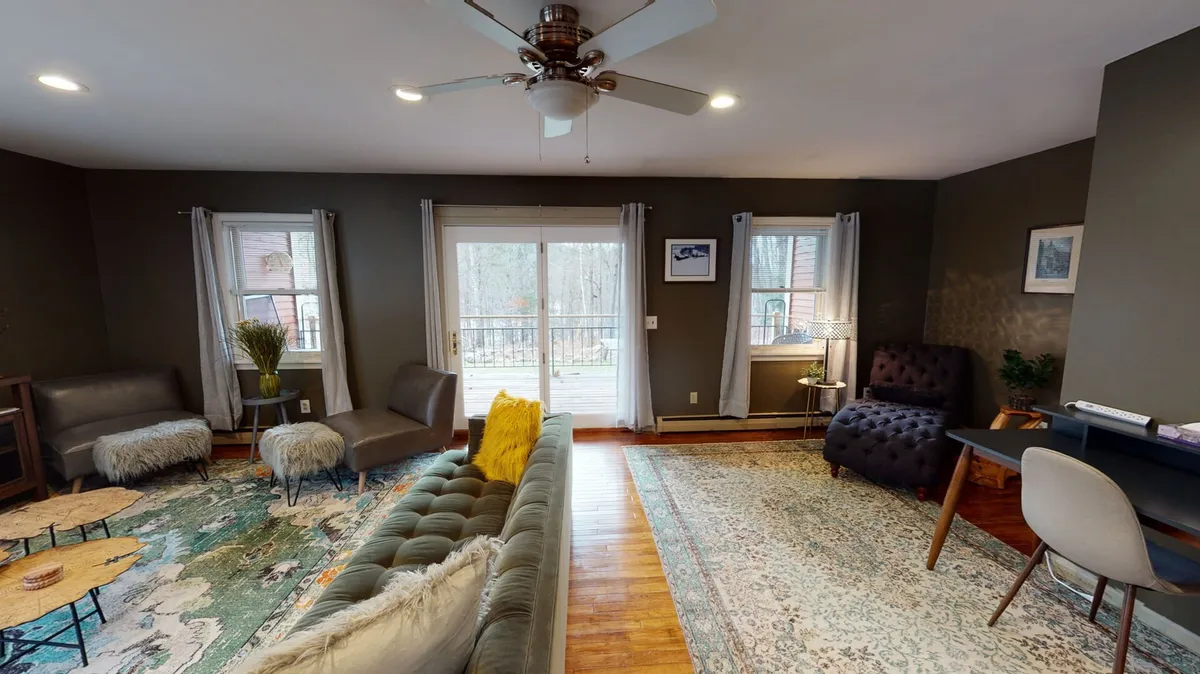 A cozy living area with a green velvet sofa, wooden coffee table, and a decorative rug. Large windows allow natural light to flood the space, highlighting the armchair and side lamp that create a perfect nook for reading or enjoying the view. The overall mood is comfortable and welcoming, ideal for unwinding at any time of day.