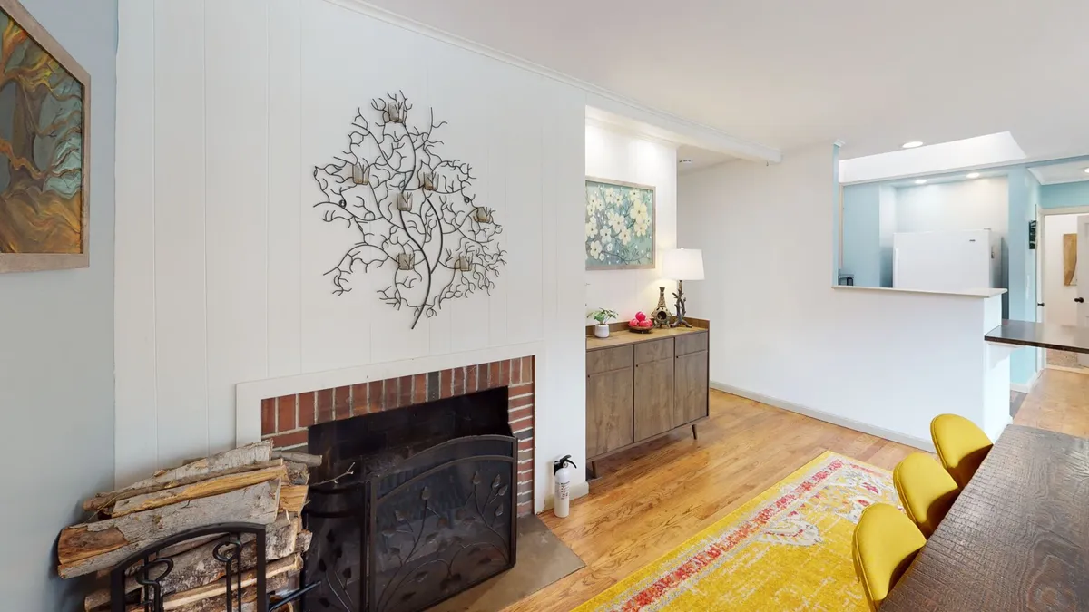 A warmly lit interior with a central fireplace, a dining table surrounded by chairs, wall art, and a vibrant rug. The space feels intimate and secluded, fostering an atmosphere of calm ideal for unwinding after a productive day or enjoying quiet, restorative moments.