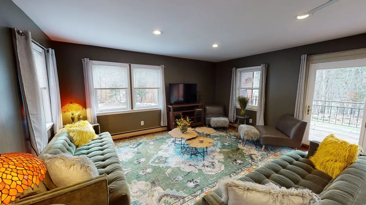 A cozy, well-lit living area featuring a sofa, rug, coffee table, windows, and a television. The layout invites group gatherings for movie nights or intimate conversations.