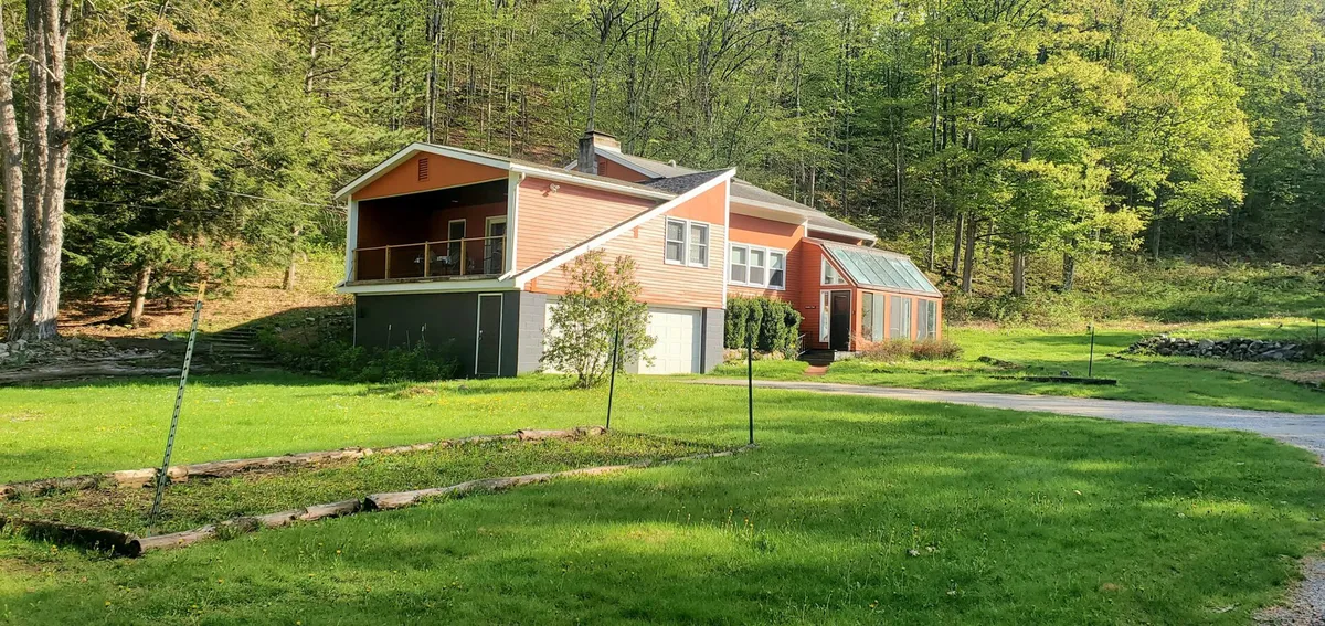 This image showcases the exterior of the house surrounded by lush green lawn, tall trees, and a clear pathway inviting exploration. The expansive yard and natural landscape are prominent, suggesting ample space for pets and their owners to roam and relax.
